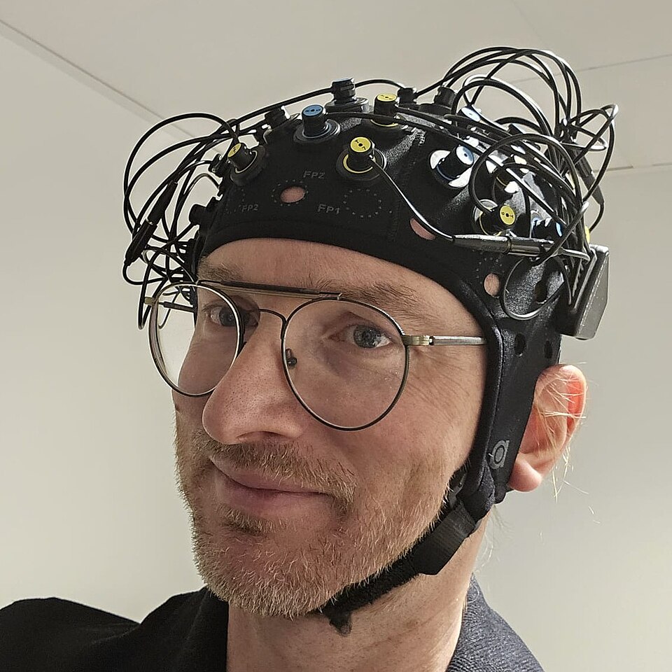 A person wearing a head cap fitted with optical fNIRS sensors and cables.